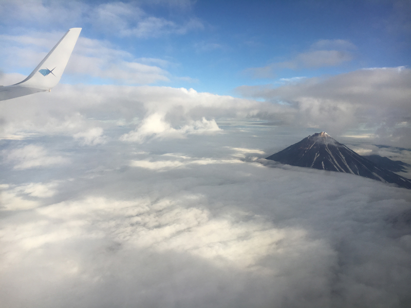 A volcano peeks through the clouds on our descent into Kamchatka. Photo credit: Jake Smith