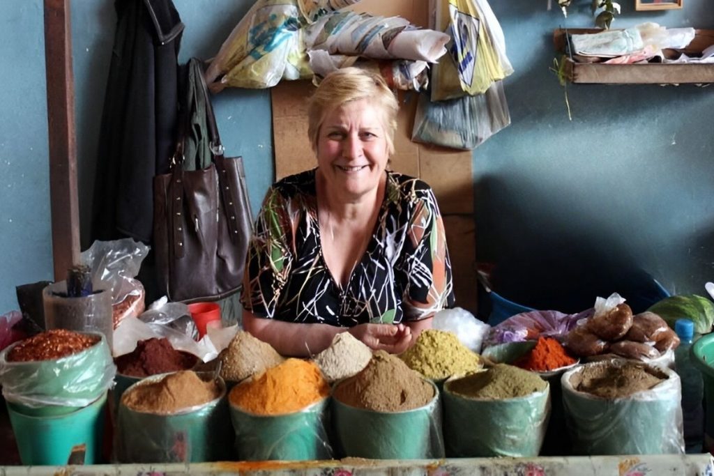 A Georgian market vendor smiling behind various spices in colorful containers. Image from trip to the South Caucasus and Türkiye by MIR Coorporation