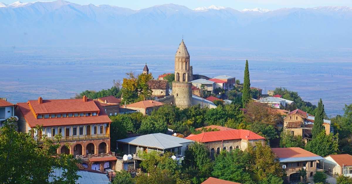 Sighnaghi, a hilltop town in Georgia, overlooks the Alazani Valley. It features red-roofed houses, lush greenery, and a historic church.